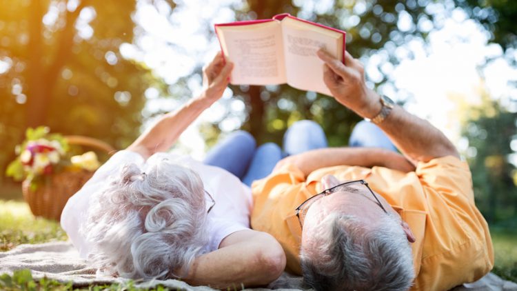 Bücher machen nicht nur schlau, sondern halten auch geistig rege - Älteres paar gemeinsam auf der Wiese liegend und lesend