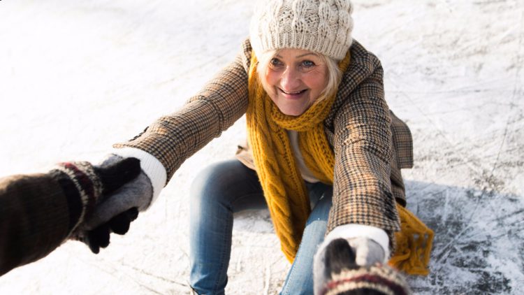 Keine Angst vor Stürzen in der kalten Jahreszeit - Ältere Frau lässt sich nach einem Sturz auf dem Eis aufhelfen