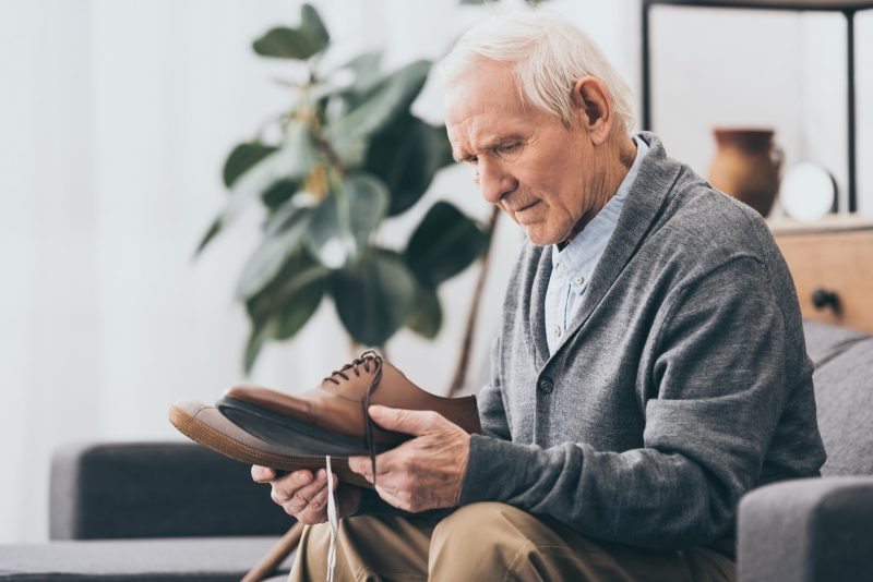 Älterer Mann sitzt und hält unterschiedliche Schuhe in den Händen