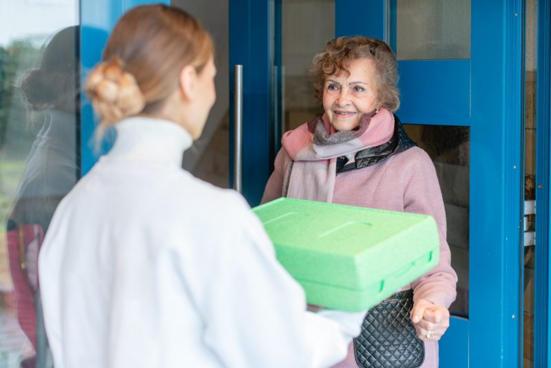 Frau bringt Seniorin Essen in einer Warmhaltebox