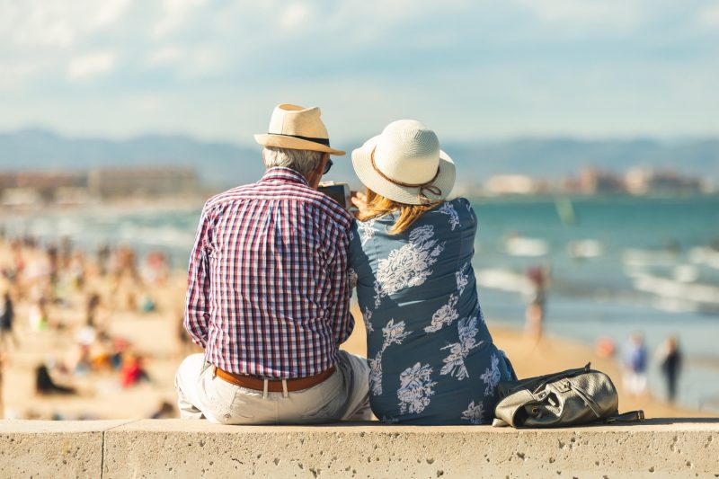 Älteres Ehepaar sitzt auf Mauer mit Blick aufs Meer