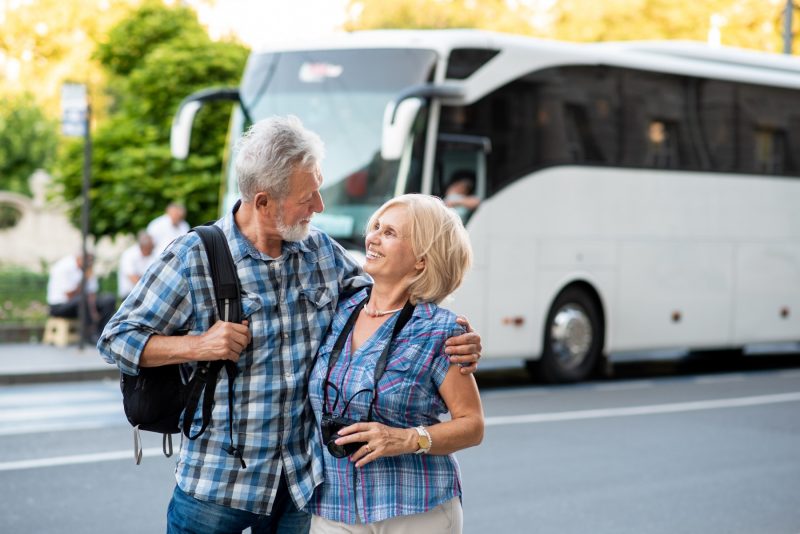Älteres Touristen-Paar mit Reisebus im Hintergrund 