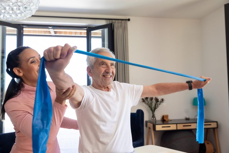 Senioren-Assistentin macht Fitness-Übungen mit älterem Mann