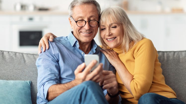 Glückliches älteres Ehepaar nutzt Smartphone