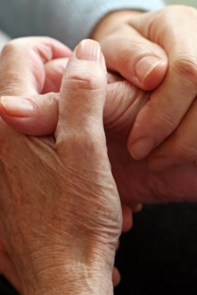 Ineinander verschränkte Hände einer älteren Personen werden von den Händen einer jüngeren Person gehalten