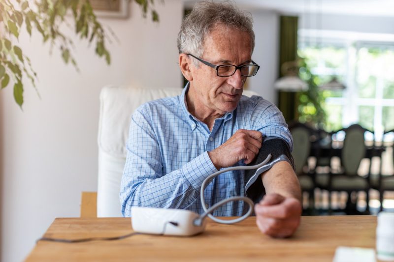 Älterer Mann legt sich die Manschette des Blutdruckmessgeräts an
