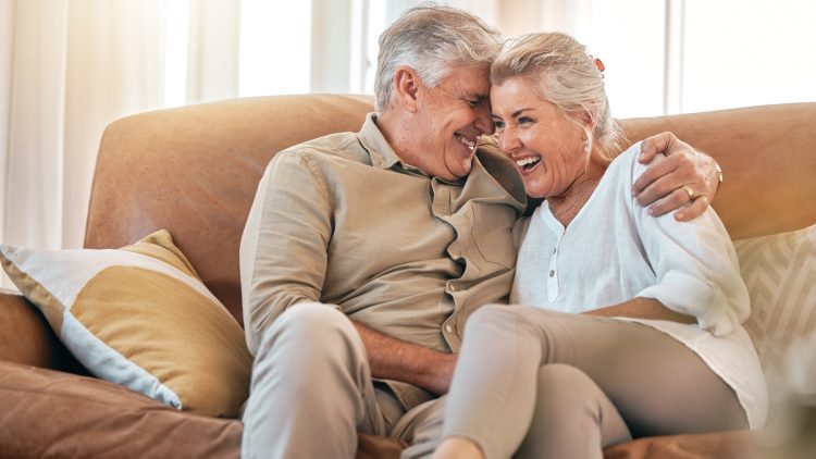 Älteres Ehepaar sitzt lachend auf Sofa