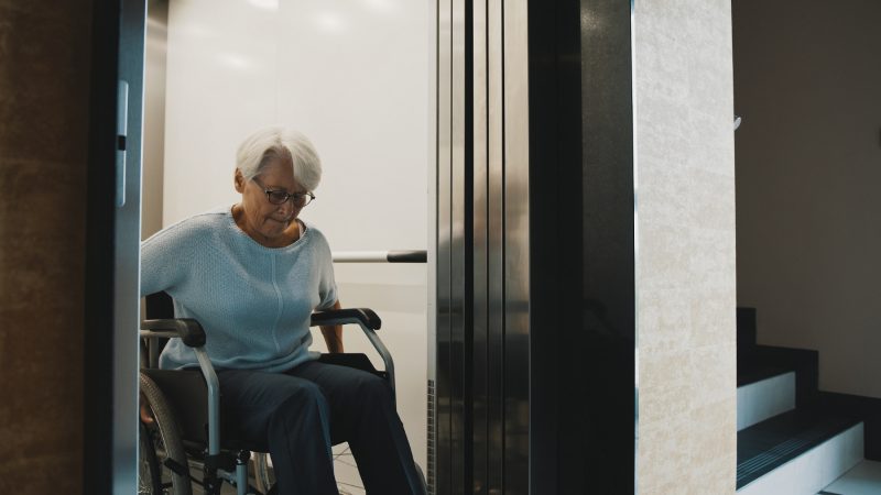 Ältere Frau im Rollstuhl nutzt Aufzug im Haus