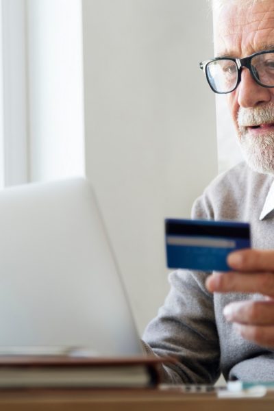 Älterer Mann sitzt am Laptop mit Girocard in der Hand