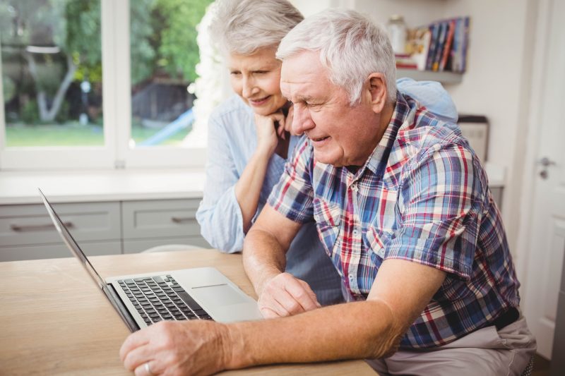 Älteres Ehepaar sitzt am Tisch vor einem Laptop für die Recherche im Internet.