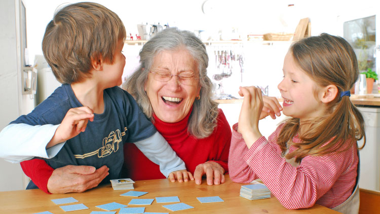 Gehirnjogging - Großmutter sitzt mit Enkelkindern in der Küche beim Memory