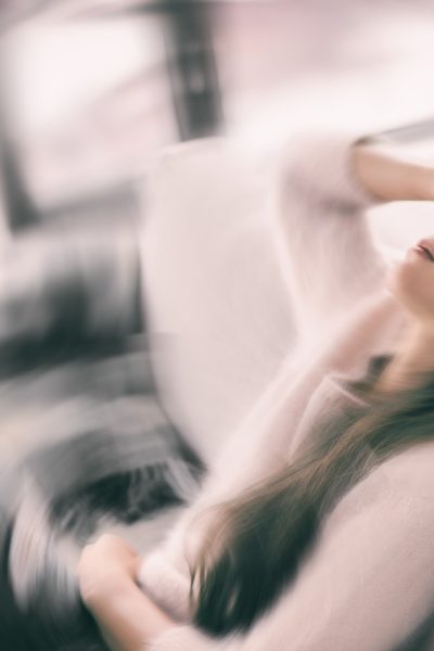 Frau sitzt mit Schmerzen zurückgelehnt auf einem Sofa Frau sitzt mit Schmerzen zurückgelehnt auf einem Sofa