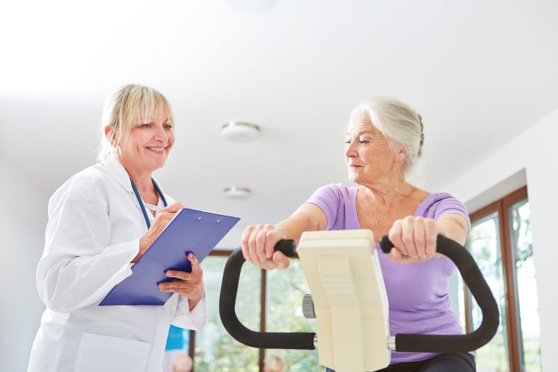 Senior Frau trainiert auf dem Ergometer beim Fitness Check betreut von Ärztin