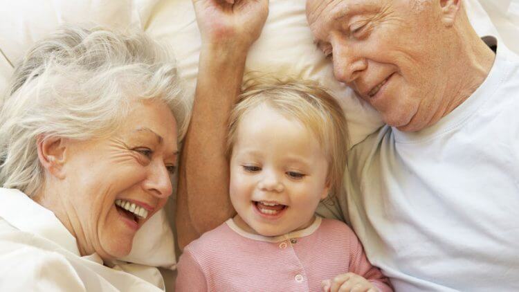 Barrierefreies Wohnen - Großeltern mit Enkeltochter beim Kuscheln im Bett