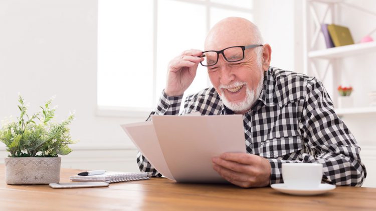Pflegekostenzuschuss beantragen - Älterer Mann schaut lächelnd auf seinen Antrag
