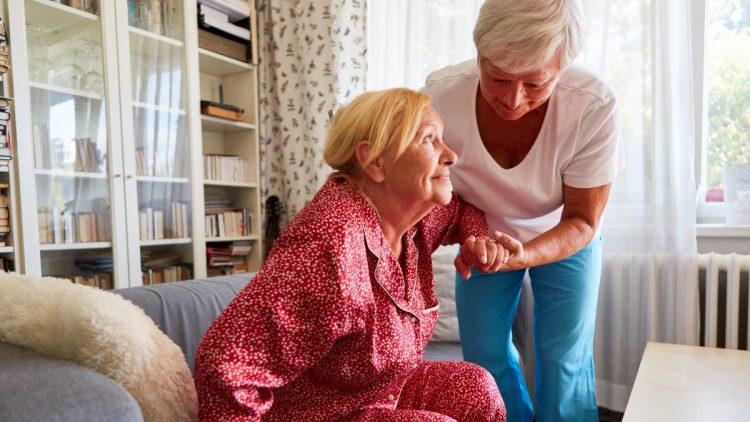 Frau hilft Seniorin beim Aufrichten vom Sofa
