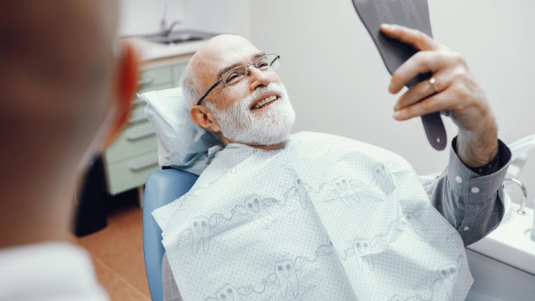 Älterer Herr betrachtet beim Zahnarzt seine Zähne im Spiegel